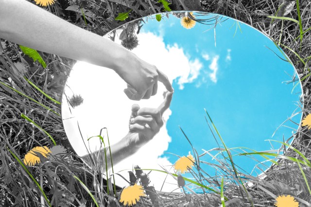 Hand pointing to its own reflection in a mirror laid in the grass